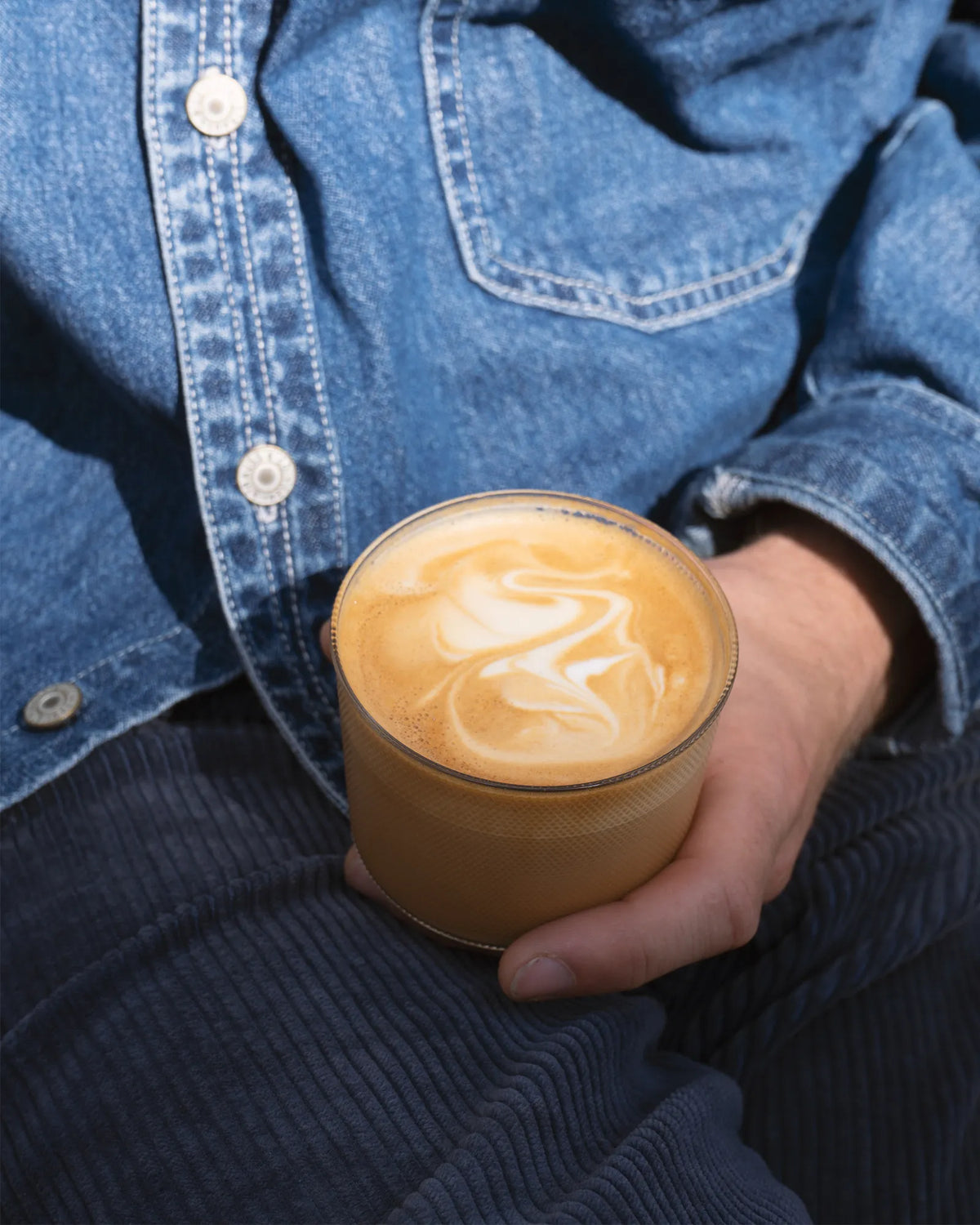 Kaffeespezialität im Café Calienna in Wien, cremiger Cappuccino mit Milchschaum-Muster, in der Hand gehalten.